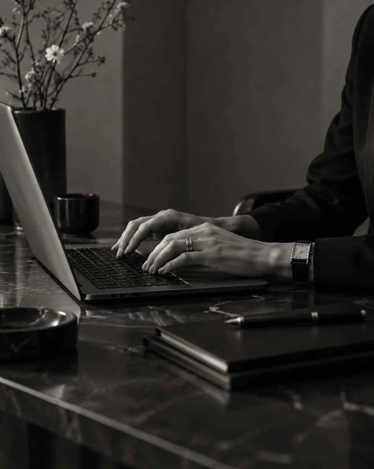 Hands working on a laptop at a dark desk, in black and white